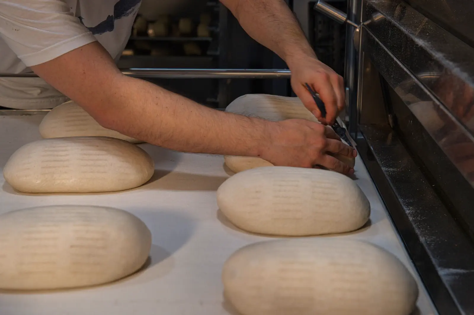 Manos dando forma a la masa de pan sobre la mesada de una panadería