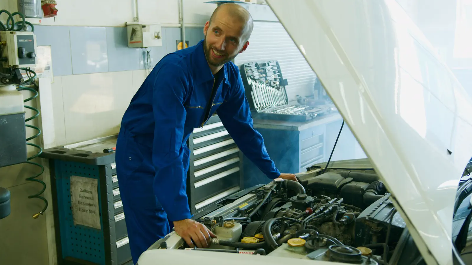 Mecánico sonriente revisando el motor de un auto en el taller